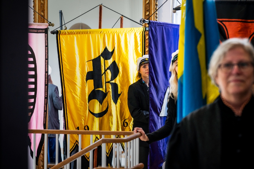 A few persons standing next to LTH's section flags. 